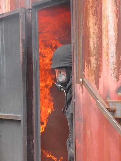 Feuerwehrmann verlässt Brandcontainer, im Hintergrund Flammen